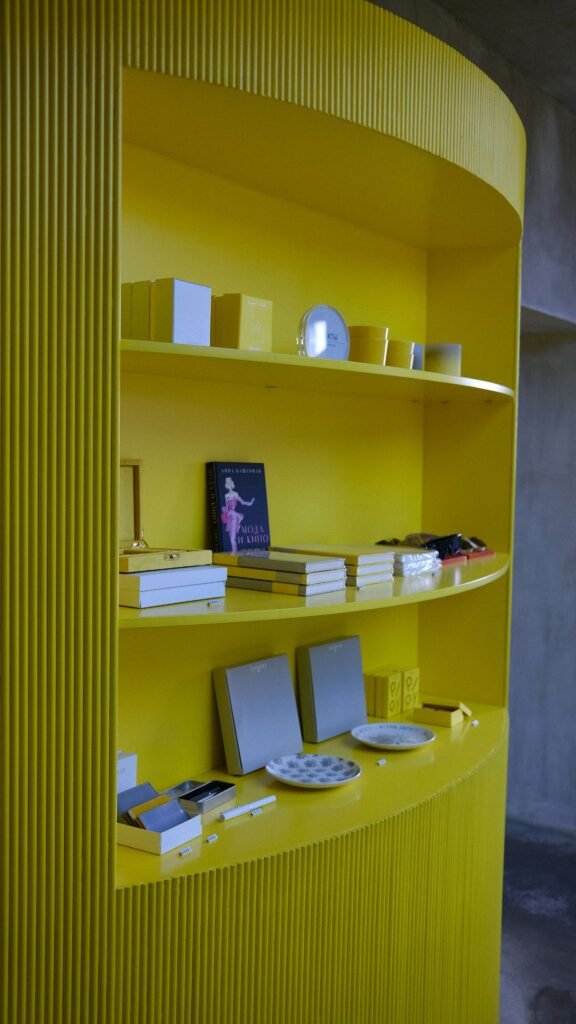 Curved yellow shelf with books, plates, and small boxes. Bright and organized display, conveying a modern and cheerful atmosphere.