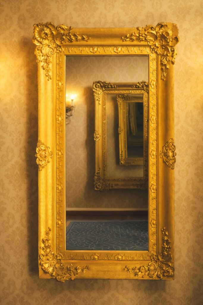 Ornate gold-framed mirror reflecting identical mirrors, creating an infinite illusion. Warm lighting with a patterned wallpaper backdrop. Elegant and timeless.